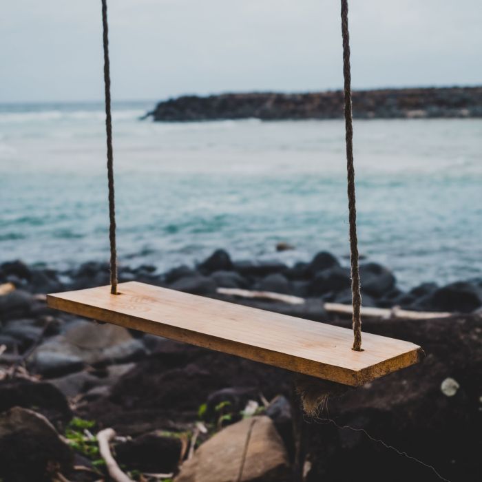 A brown wooden swing chair beside shoreline.