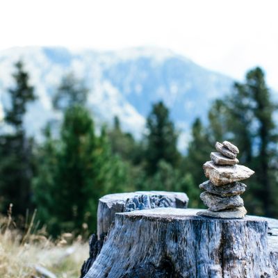 a pile of little stones are stacked vertically on a rock. in the background are green trees and snowy mountains