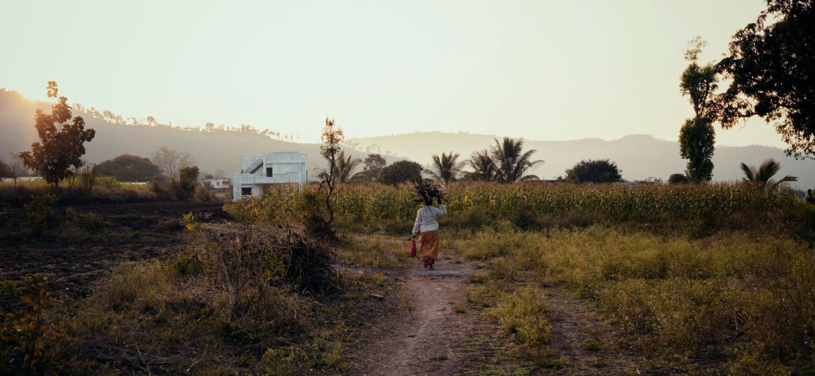 A person walking down a dirt path in a field in a visibly rural area.