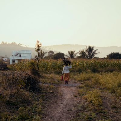 A person walking down a dirt path in a field in a visibly rural area.