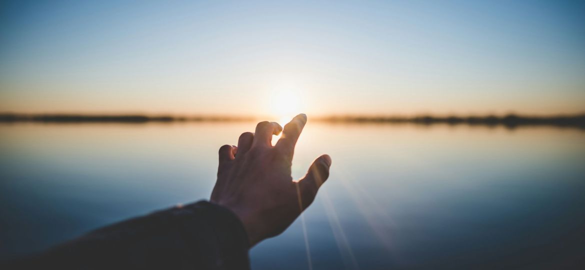 landscape photography of person's hand in front of sun