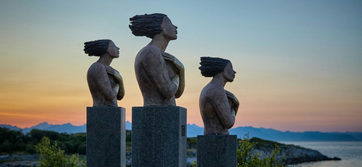 three concrete sculptures resembling human figures installed at a high altitude and facing towards the right of the image.