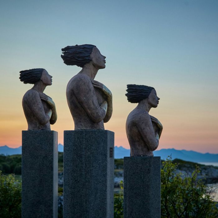 three concrete sculptures resembling human figures installed at a high altitude and facing towards the right of the image.