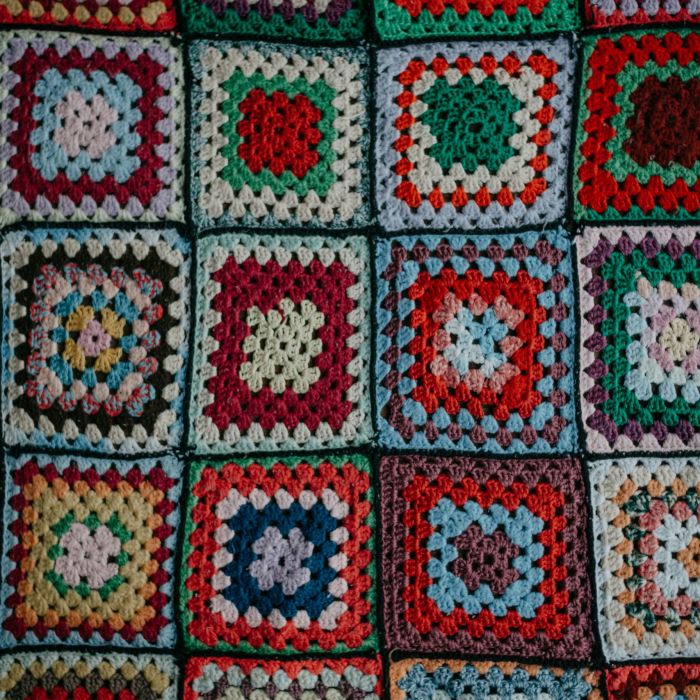 A close-up of a crocheted blanket formed of vibrant squares of knitted fabric.