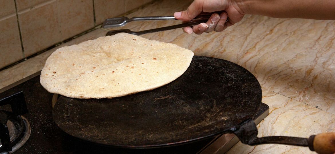 Person holding stainless steel tong and cooking a roti on a tawa.