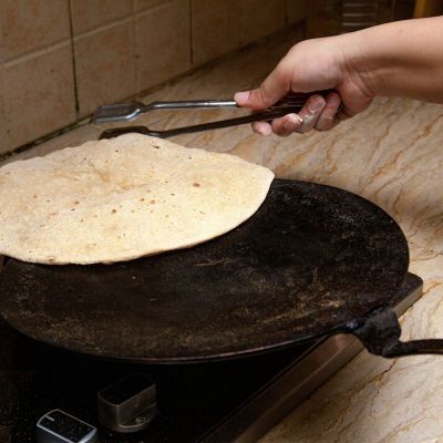 Person holding stainless steel tong and cooking a roti on a tawa.