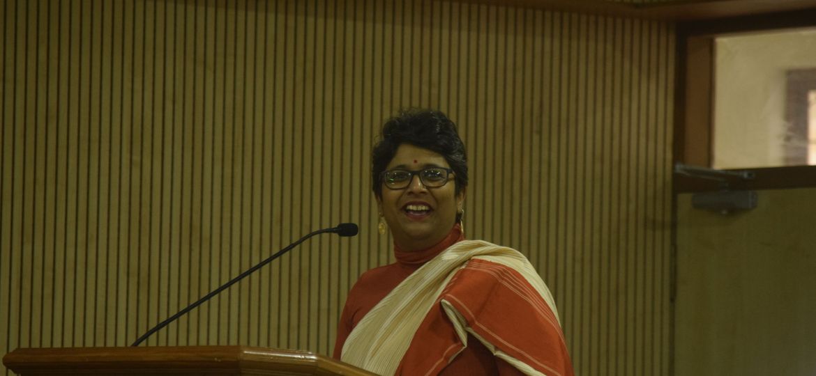 A photo of Ketaki Chowkhani standing at a podium and dressed in a sari.