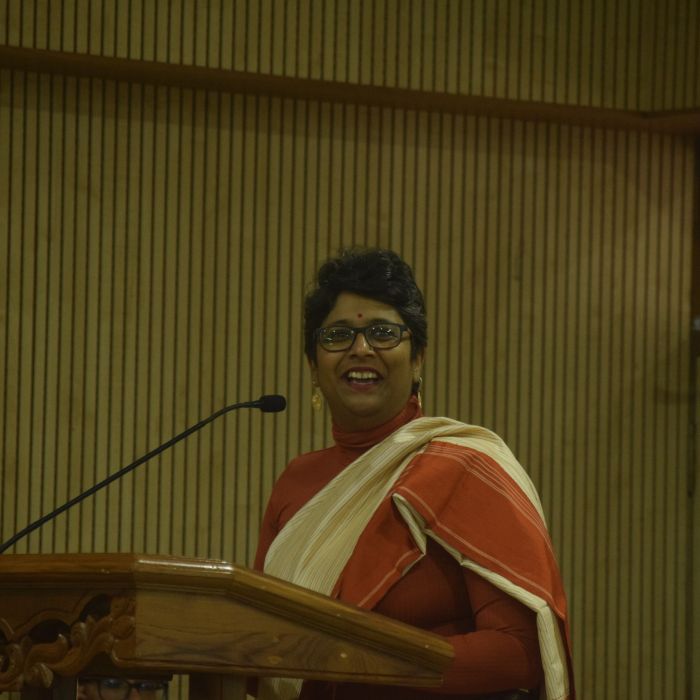 A photo of Ketaki Chowkhani standing at a podium and dressed in a sari.