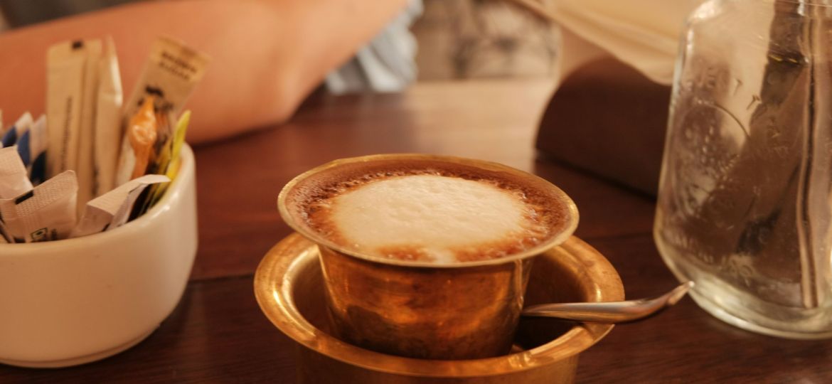 A serving of filter coffee in brass tumbler on a wooden table.