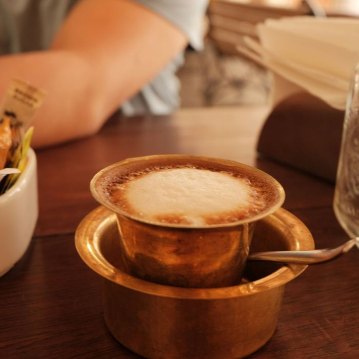 A serving of filter coffee in brass tumbler on a wooden table.